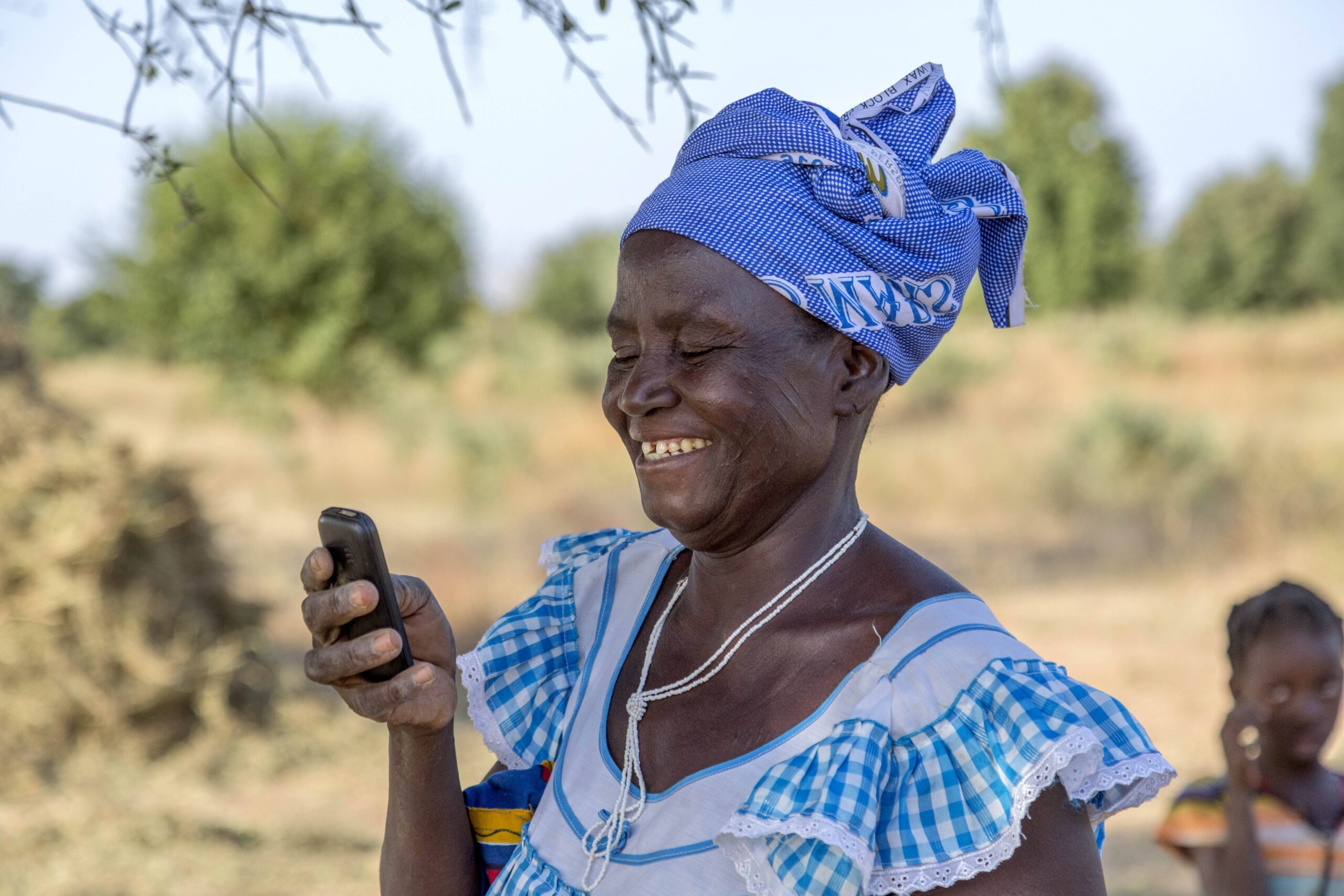 A woman farmer dressed in blue checks a mobile phone in Burkina Faso